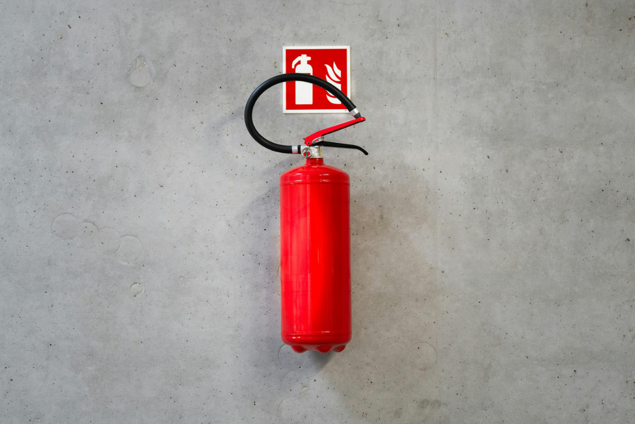 A red fire extinguisher mounted on a gray wall below a fire extinguisher sign.